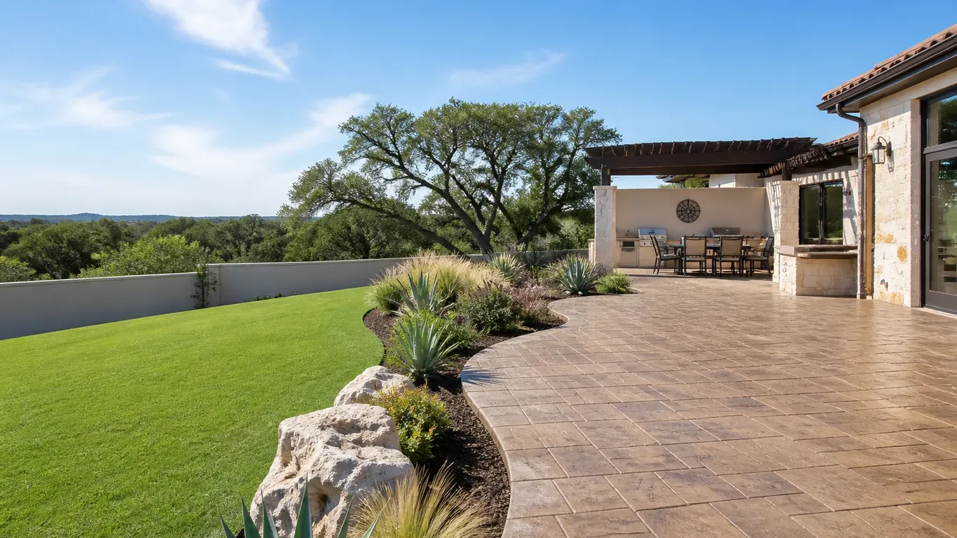 Stamped concrete patio and covered outdoor kitchen beside a lawn with a hill-country view