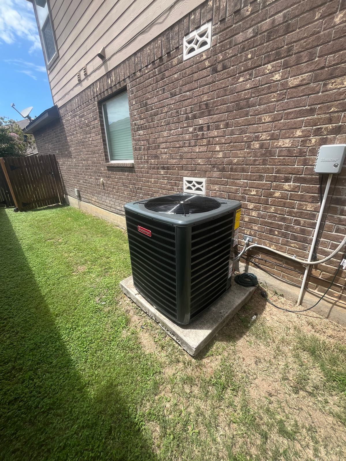 Condensing unit on a pad in a side yard beside a brick wall with its disconnect