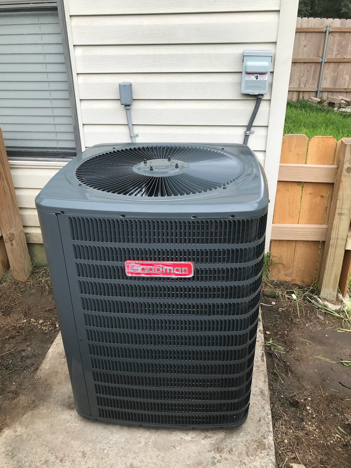 Goodman outdoor condensing unit on a pad beside siding with its disconnect and whip