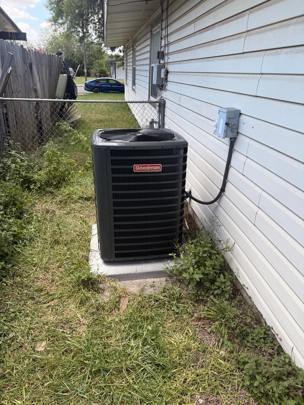 Goodman outdoor condensing unit on a new concrete pad with a disconnect and liquid-tight whip on the wall