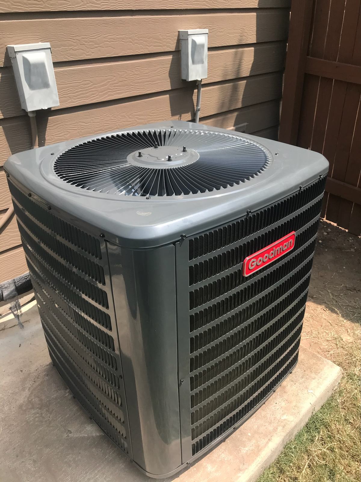 Goodman condensing unit on a pad with two disconnects on the wall above it