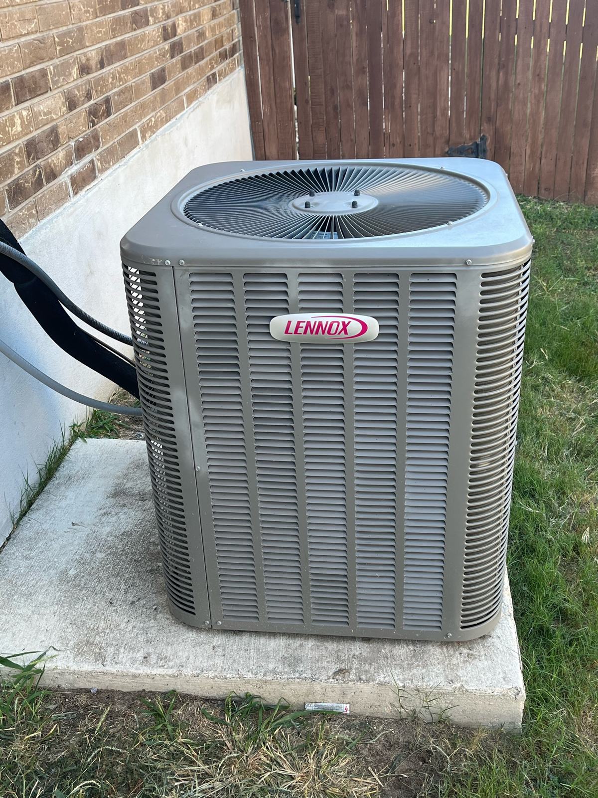 Lennox outdoor condensing unit on a concrete pad beside a brick wall and wood fence