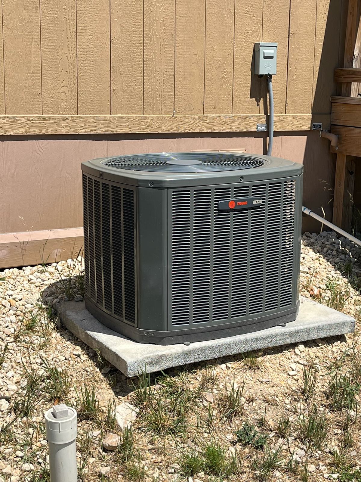 Trane outdoor condensing unit on a pad in a gravel bed with a disconnect and conduit whip on the wall