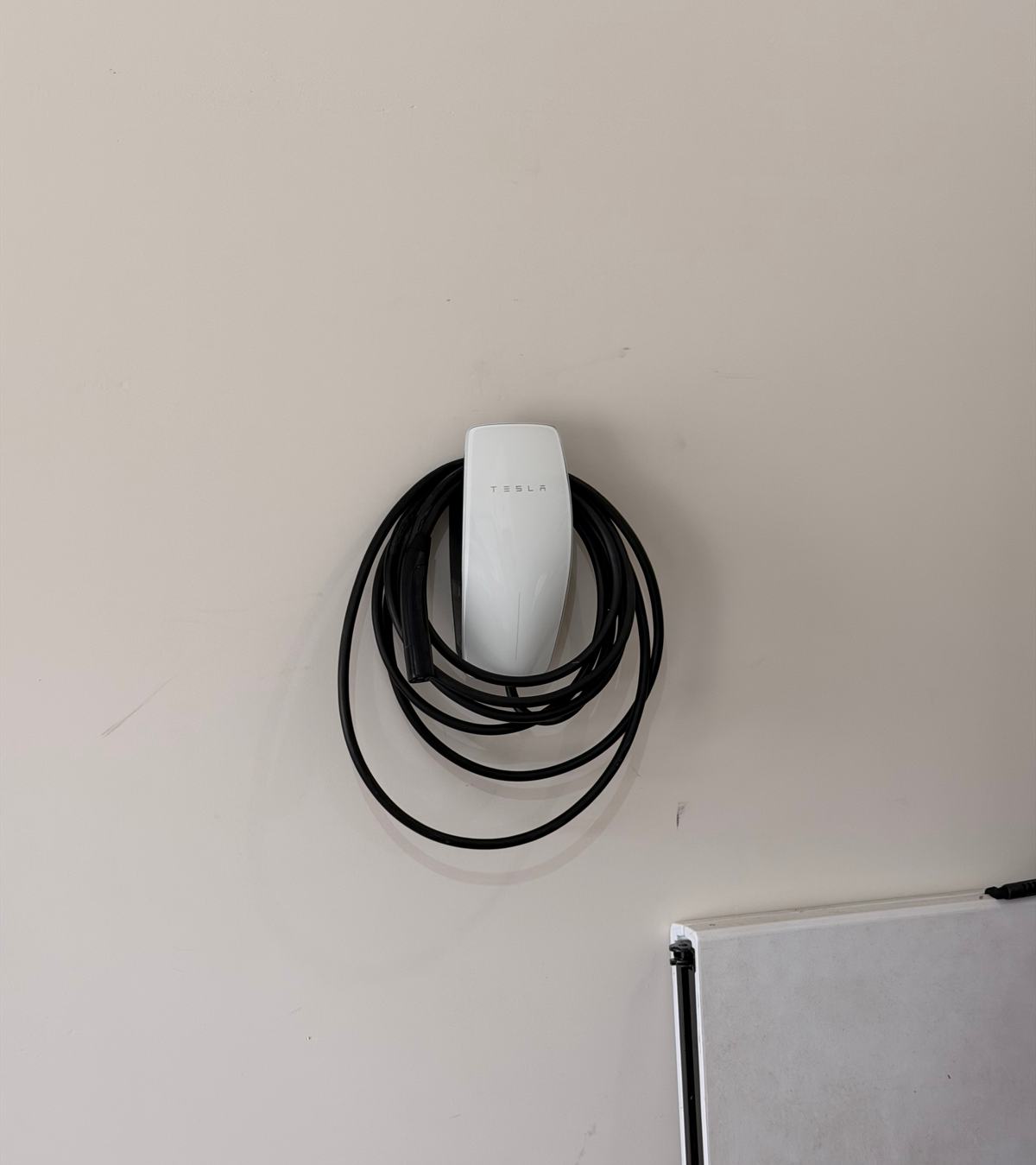 White wall-mounted EV charger with its charging cable coiled around it on a clean garage wall