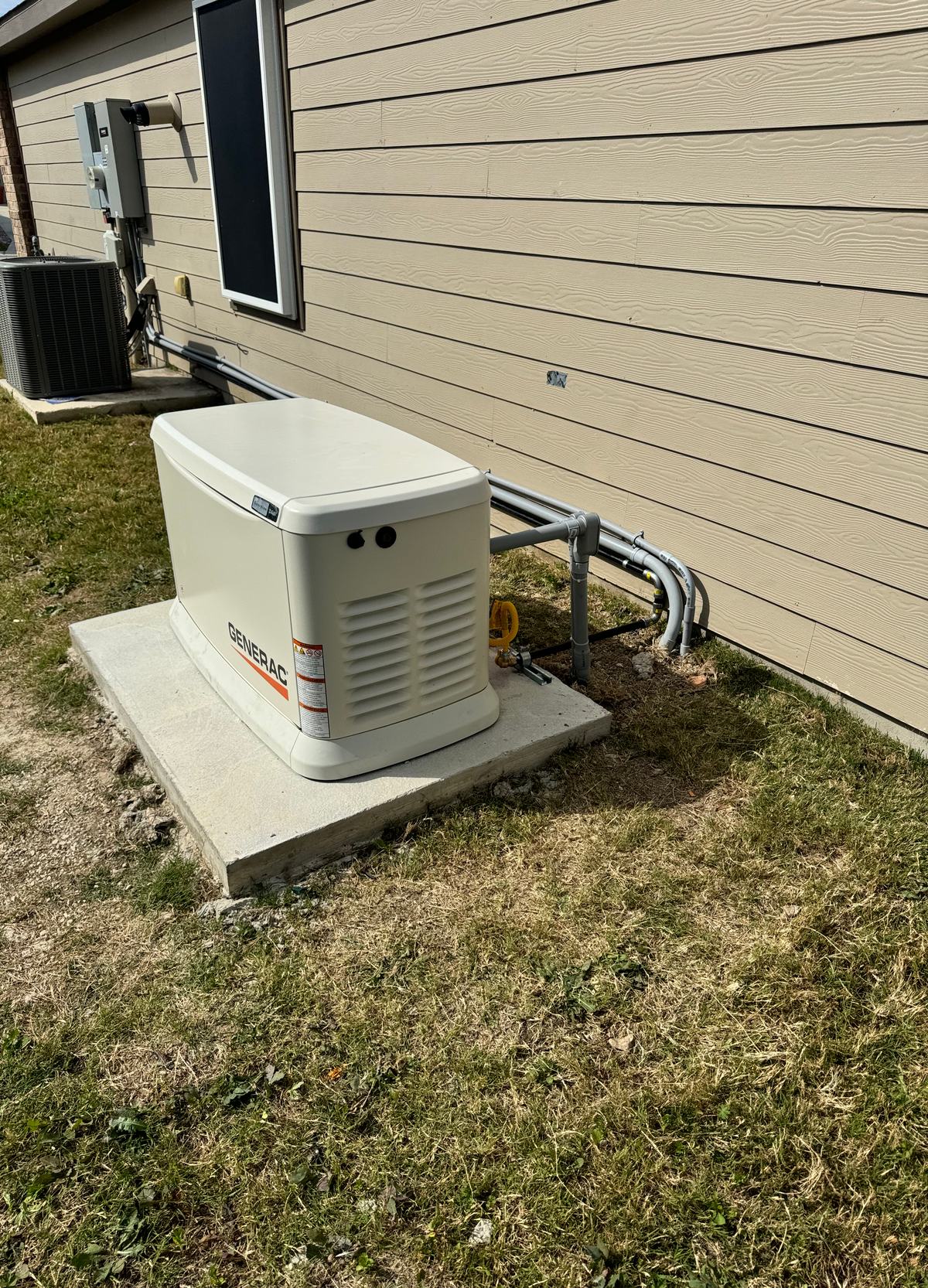 Standby generator on a concrete pad beside a siding wall, with conduit and gas piping