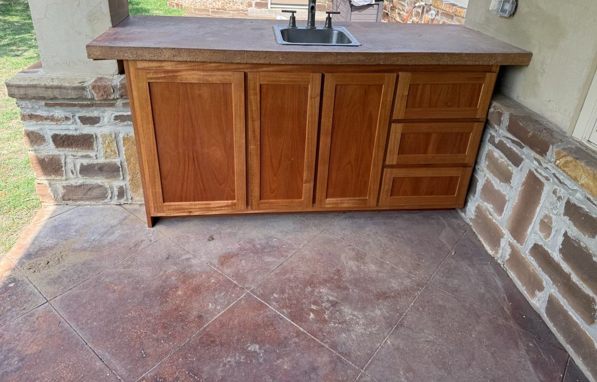 Covered patio cabinet with shaker doors and a three-drawer bank under a poured concrete top with a bar sink