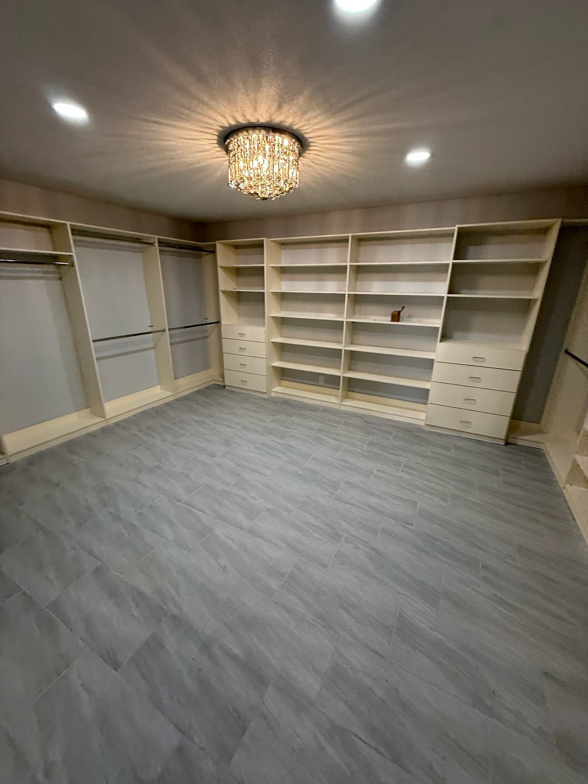 Walk-in closet lined with built-in shelving, drawer banks and hanging sections under a crystal ceiling light