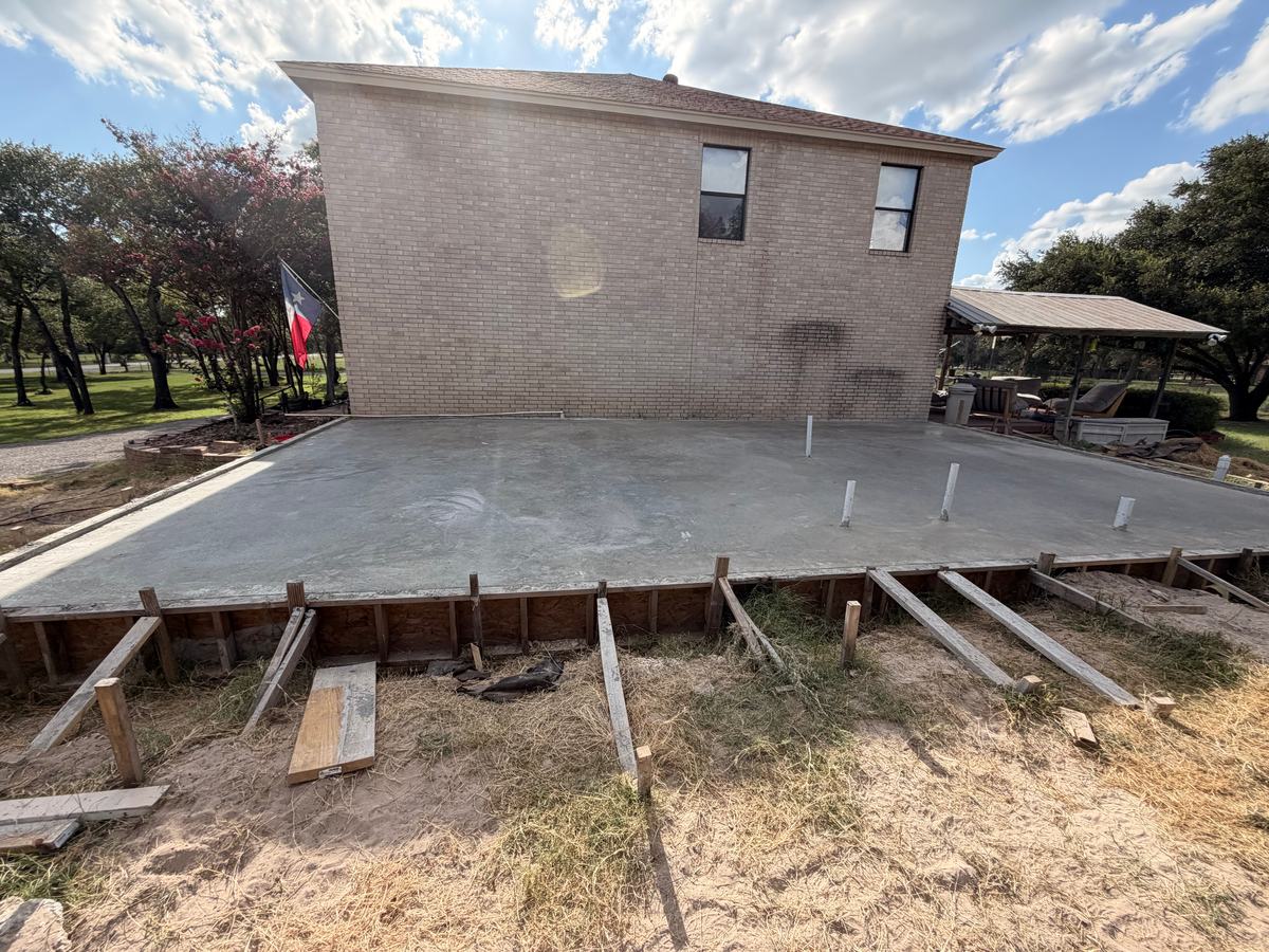 Freshly poured concrete slab along a two-story brick house, still in its wood forms