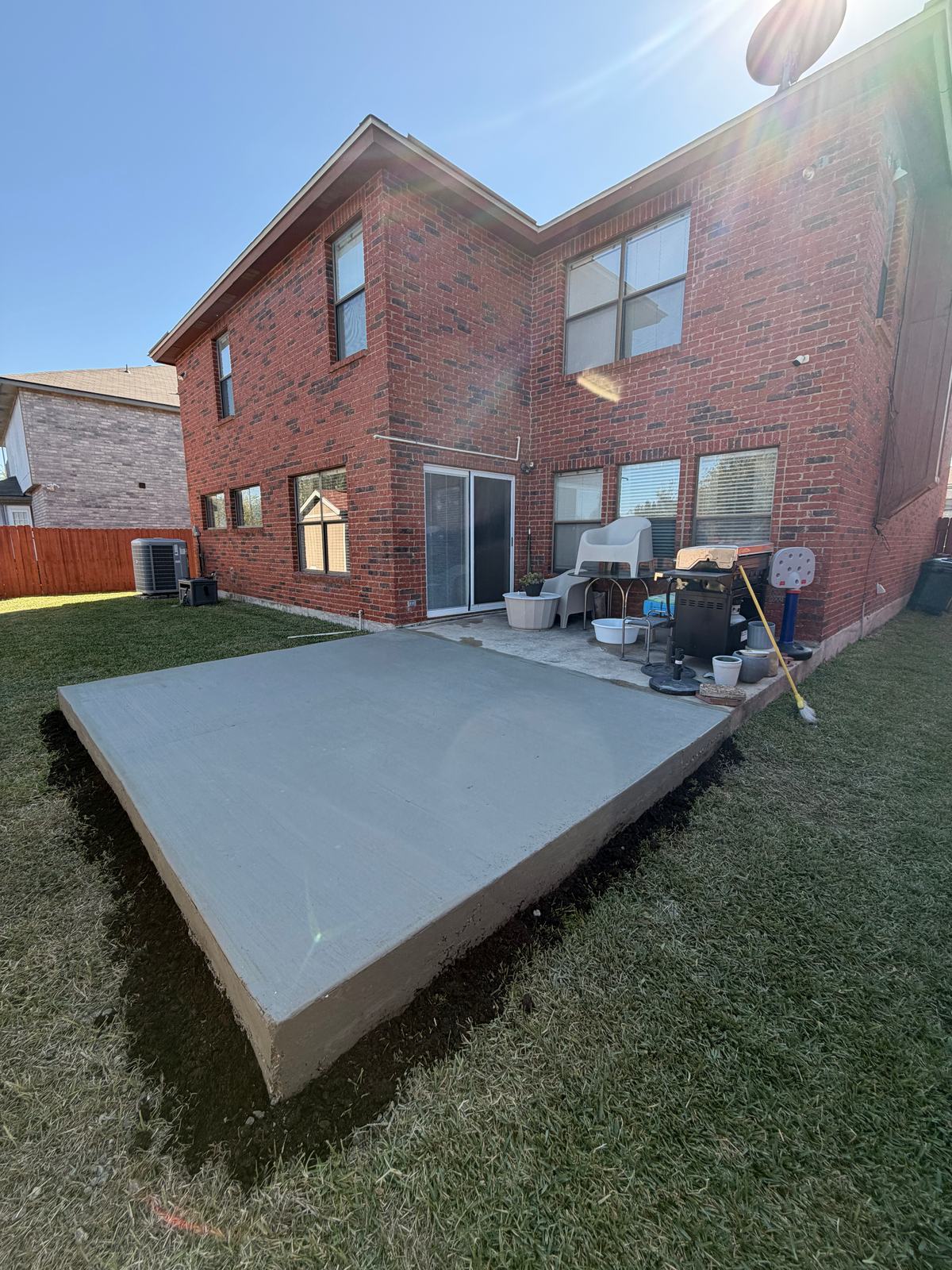 Concrete patio slab extension reaching into the lawn beside a two-story brick house
