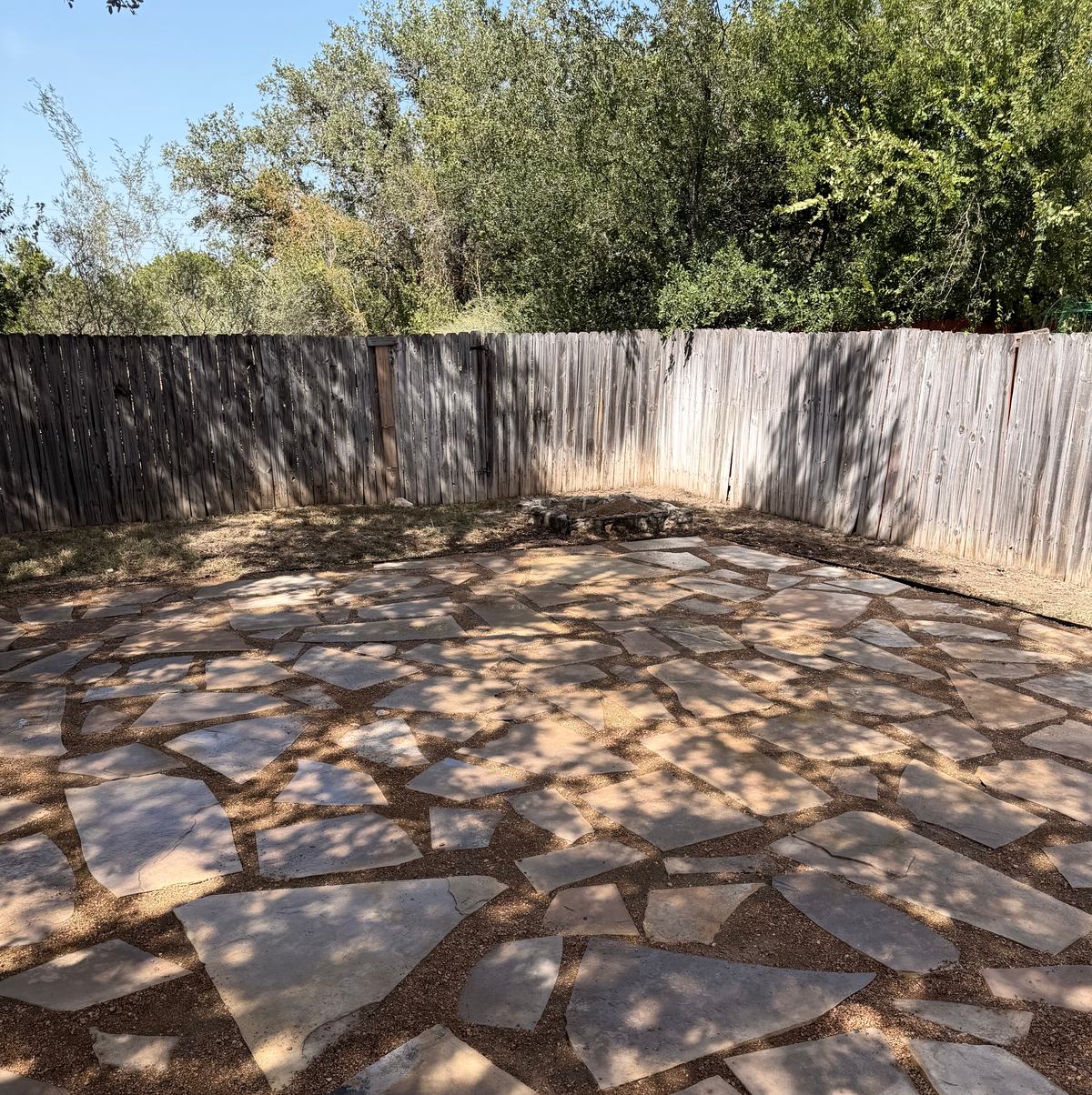 Flagstone patio set in decomposed granite inside a wood privacy fence, with a stone fire ring in the far corner