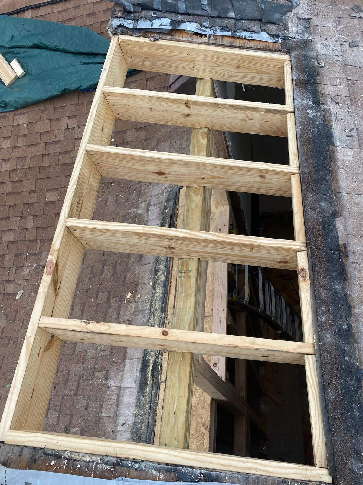 New wood rafter framing set into an opening in a shingle roof, seen from above