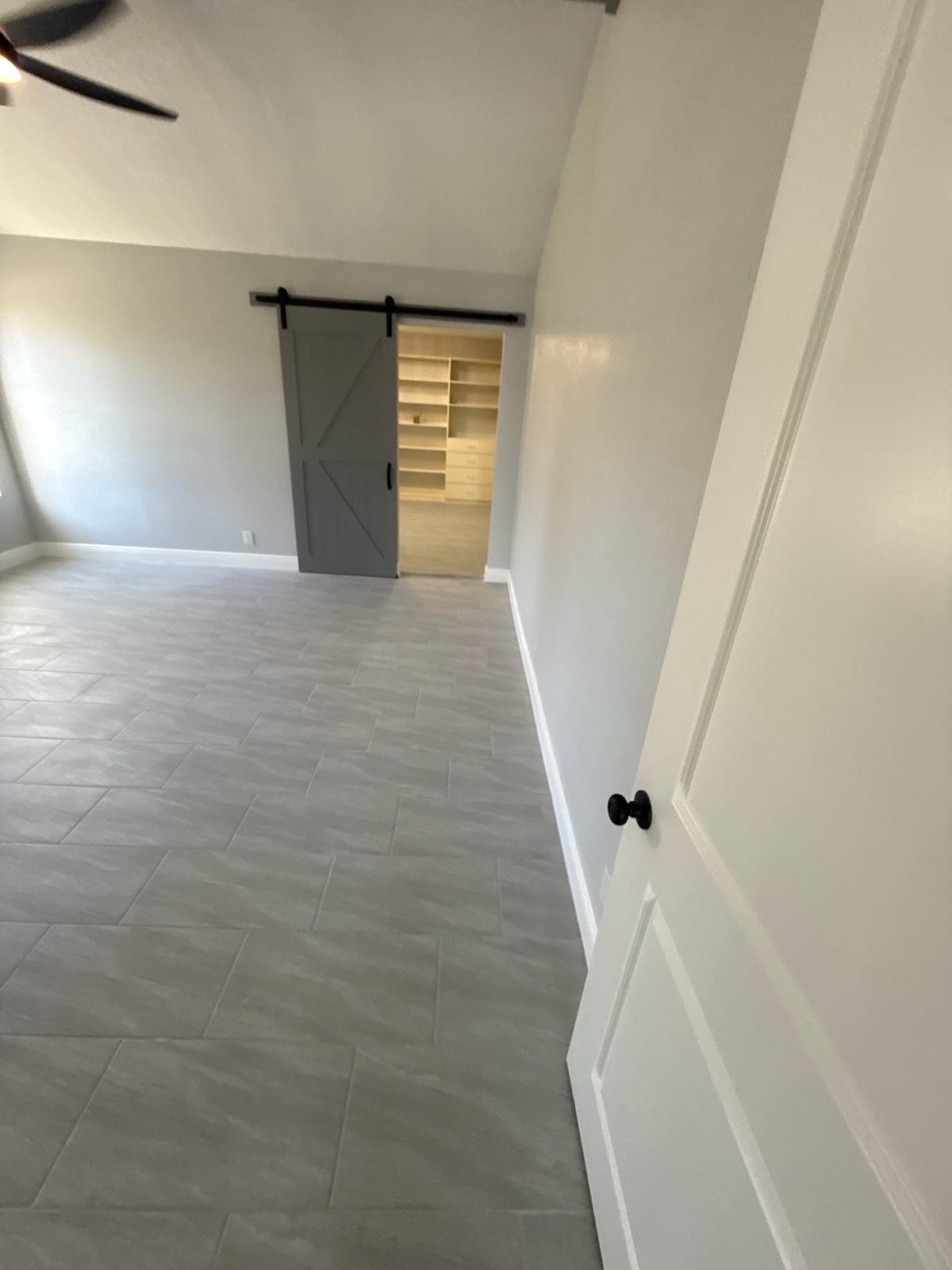 Grey barn door slid open to closet shelving in a room with a large-format tile floor