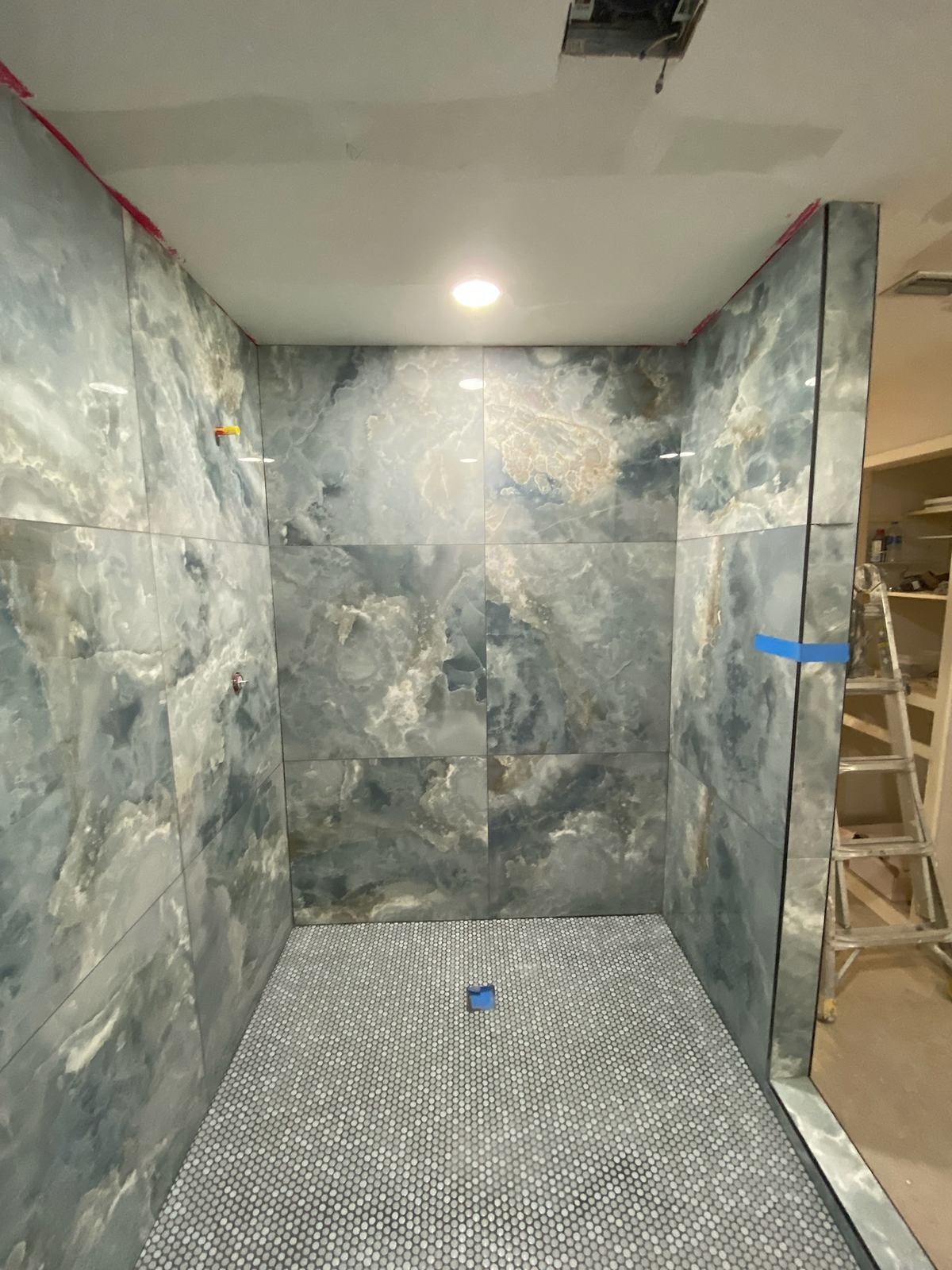 Large blue-grey marble-look tile set on shower walls over a penny-round floor before the glass and trim