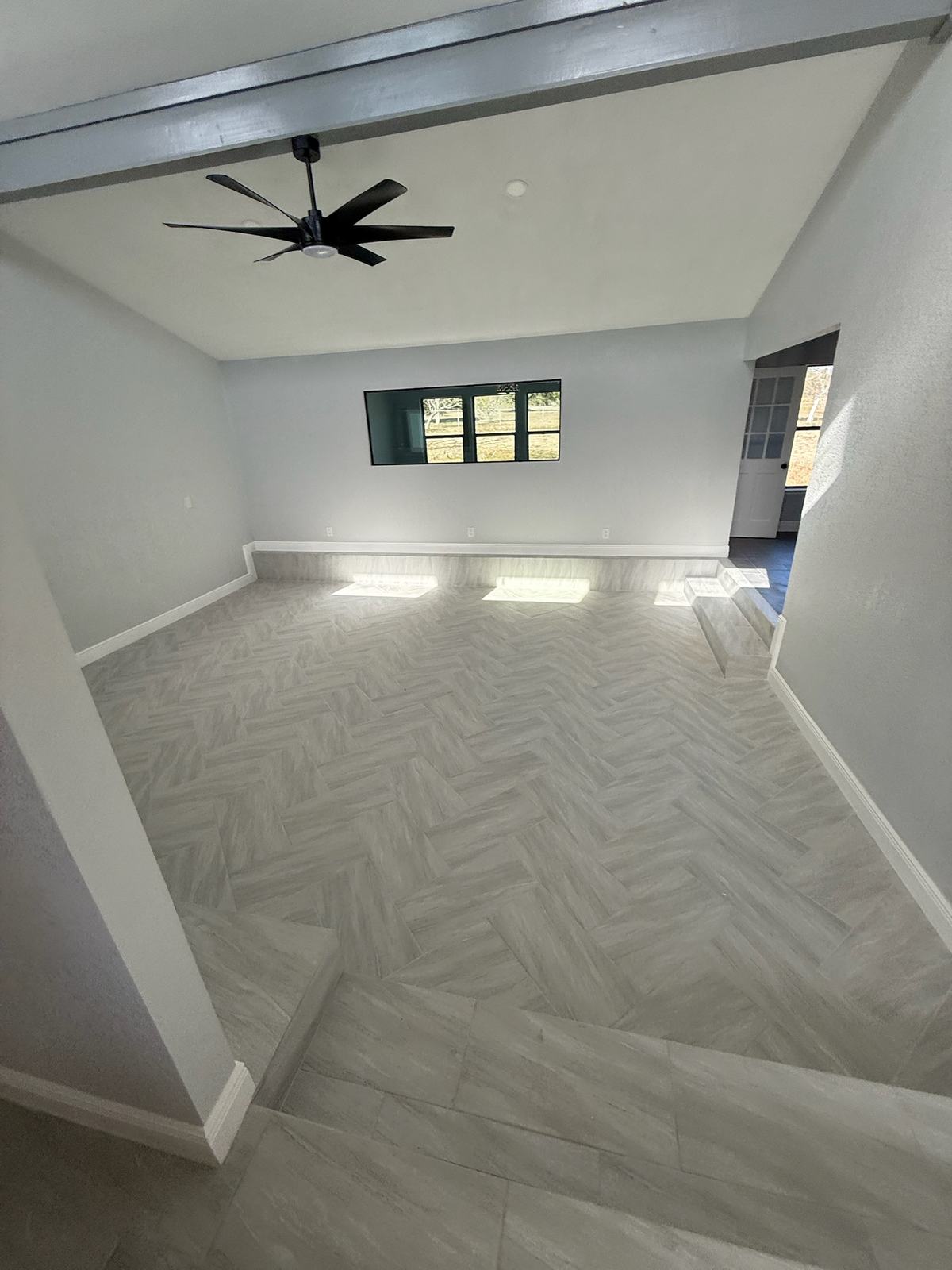 Bright room with a herringbone plank tile floor, a painted beam, a step-down and a ceiling fan
