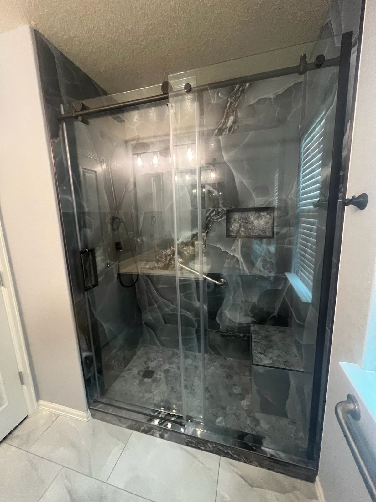 Walk-in shower with onyx-look tile, a niche, a tiled bench and bronze-framed sliding glass doors