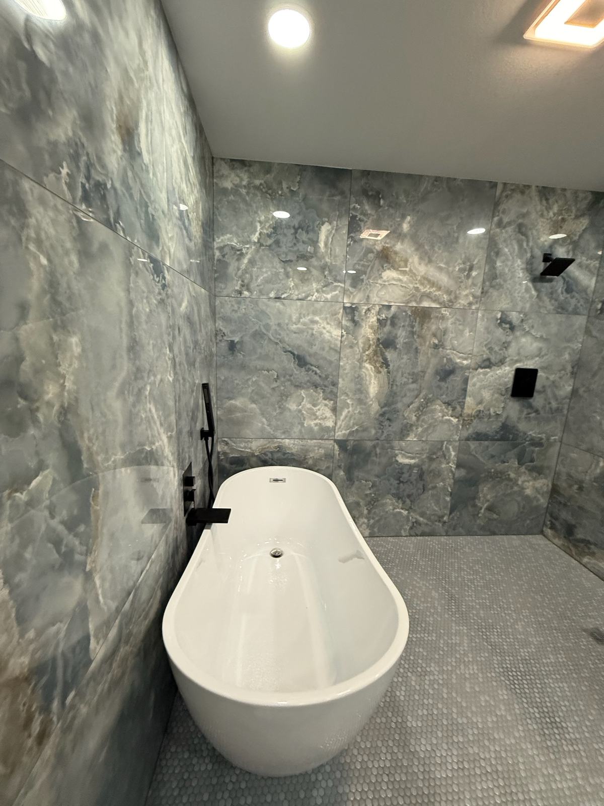 Wet room with large blue-grey marble-look tile, a penny-round floor and a freestanding tub