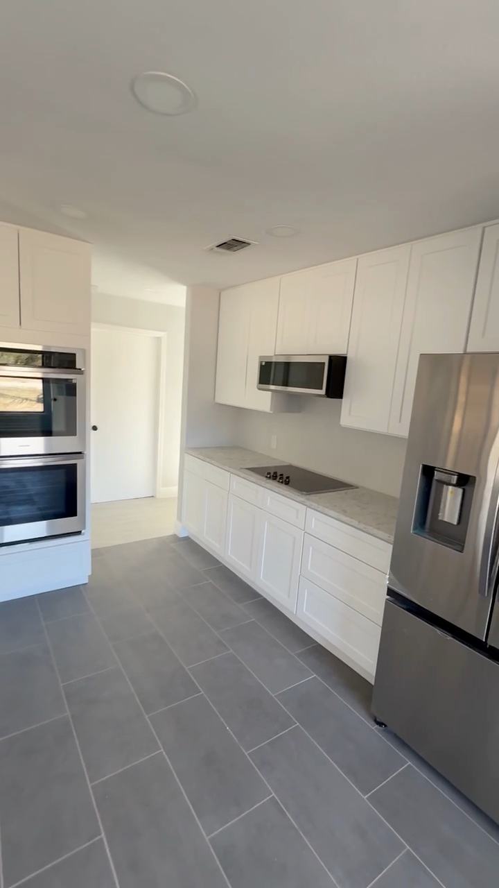 White kitchen with shaker cabinets, wall ovens, a cooktop and a large-format tile floor