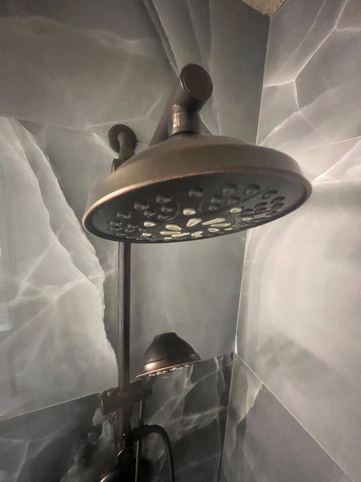 Bronze rain shower head and handheld shower on onyx-look tile